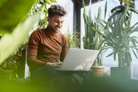 Mann sitzt mit Laptop auf dem Boden und arbeitet an nachhaltigen Digitalisierungslösungen.